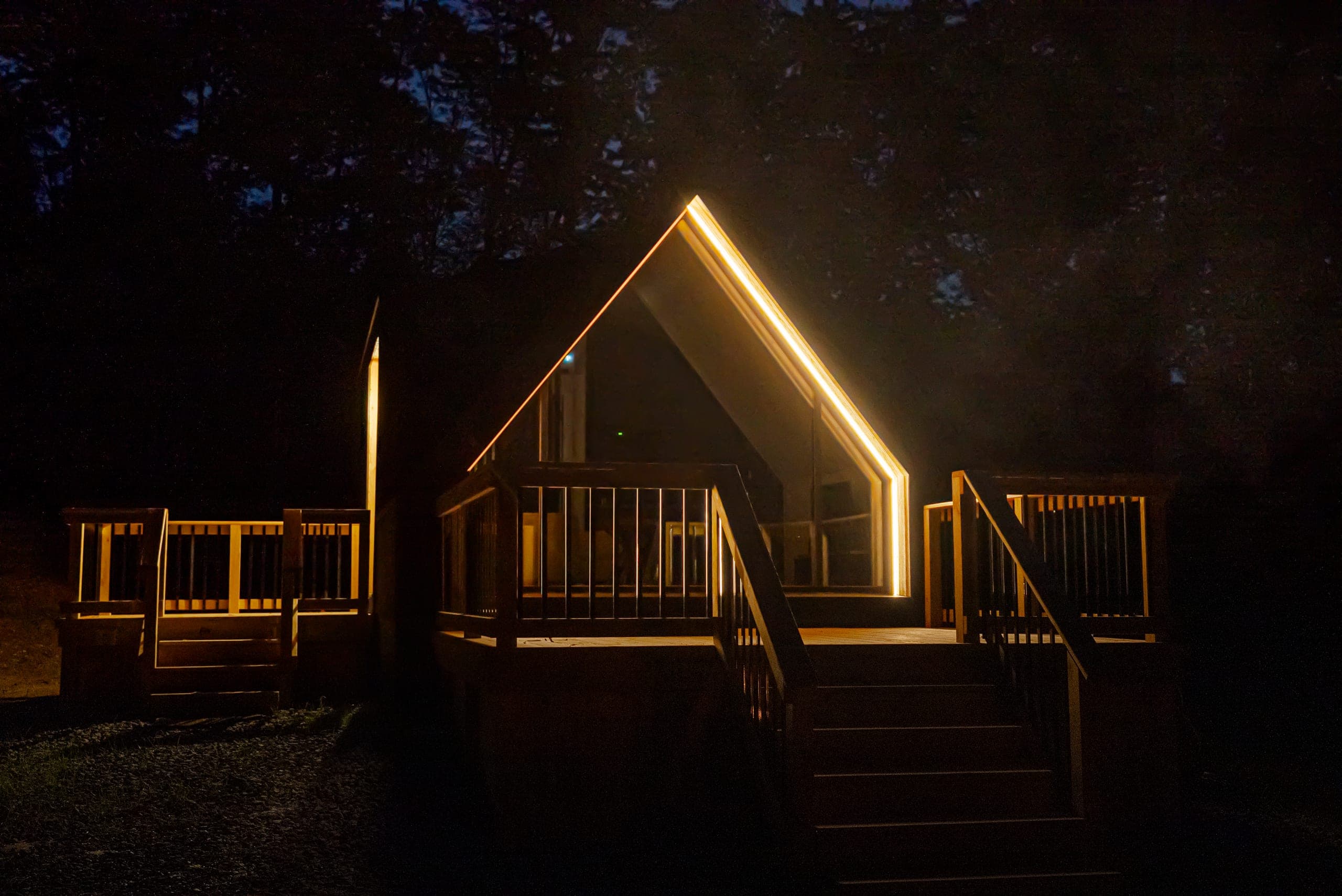 The cabin at night, its roofline traced in warm light, with a fire burning in the fire pit
